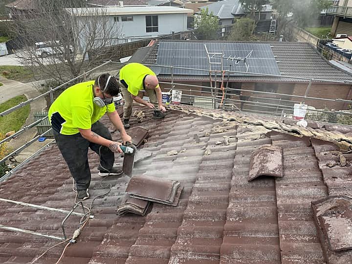Two roofers grinding out old mortar along a ridge line before re-bedding
