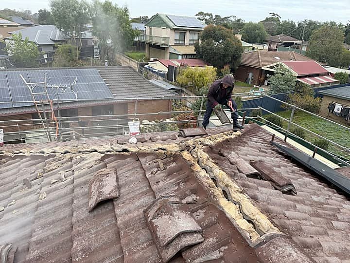 Roofer lifting old ridge caps and stripping back perished bedding mortar
